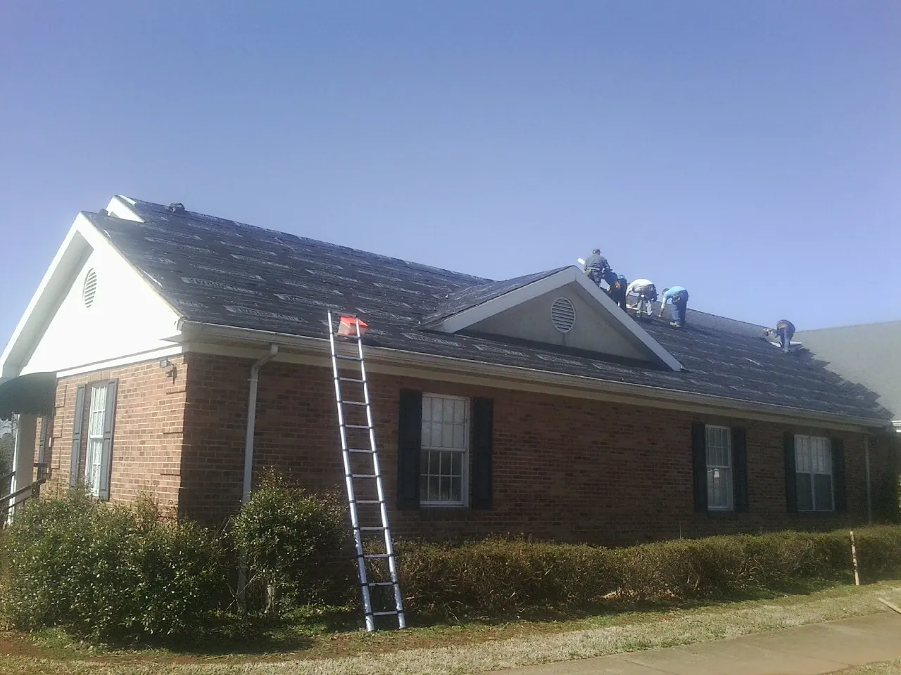 Crew tearing shingles off a brick ranch roof with a ladder set — Emergency Roof Repair work by our crew in Coalton