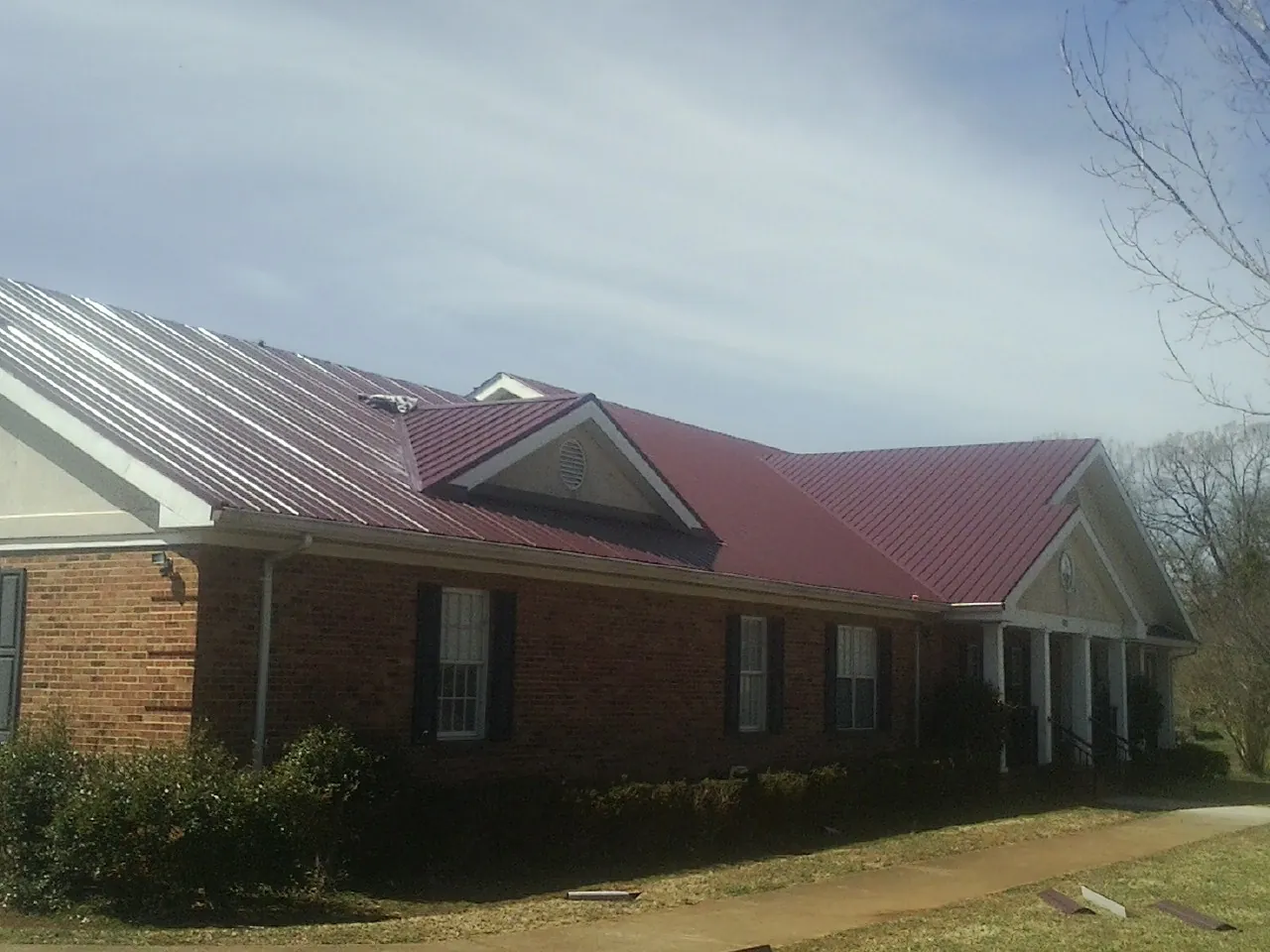 Red metal roof with gabled entries on a long brick building, from a Hail Damage Roof Repair job in Coalton
