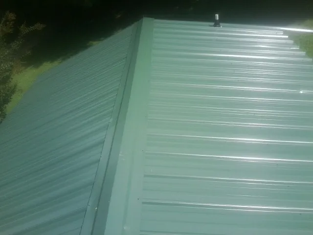 New green metal panels meeting at the ridge of a roof — Flat Roof Repair work by our crew in Coalton