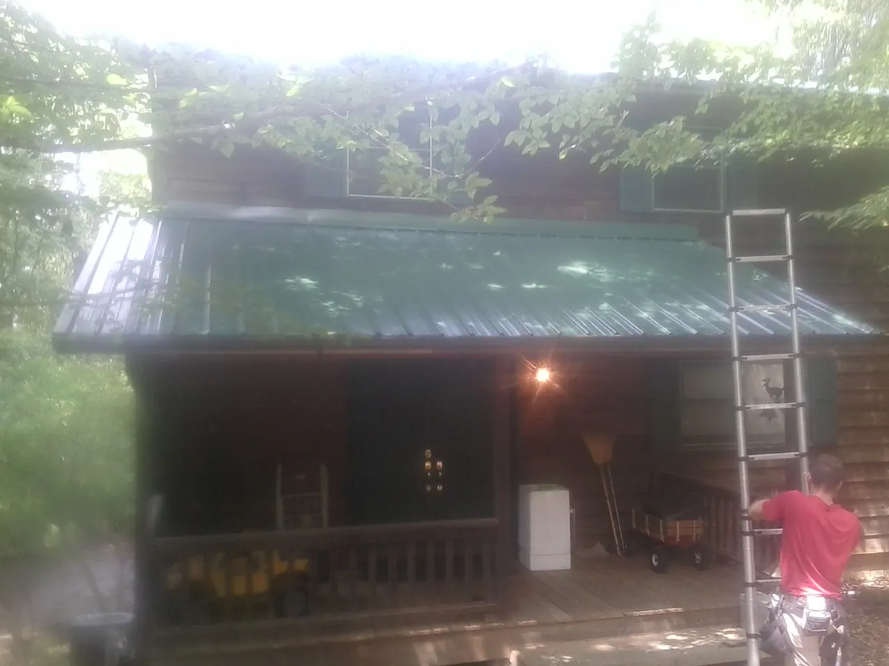 Worker on a ladder at the green porch roof of a wooded cabin in Coalton