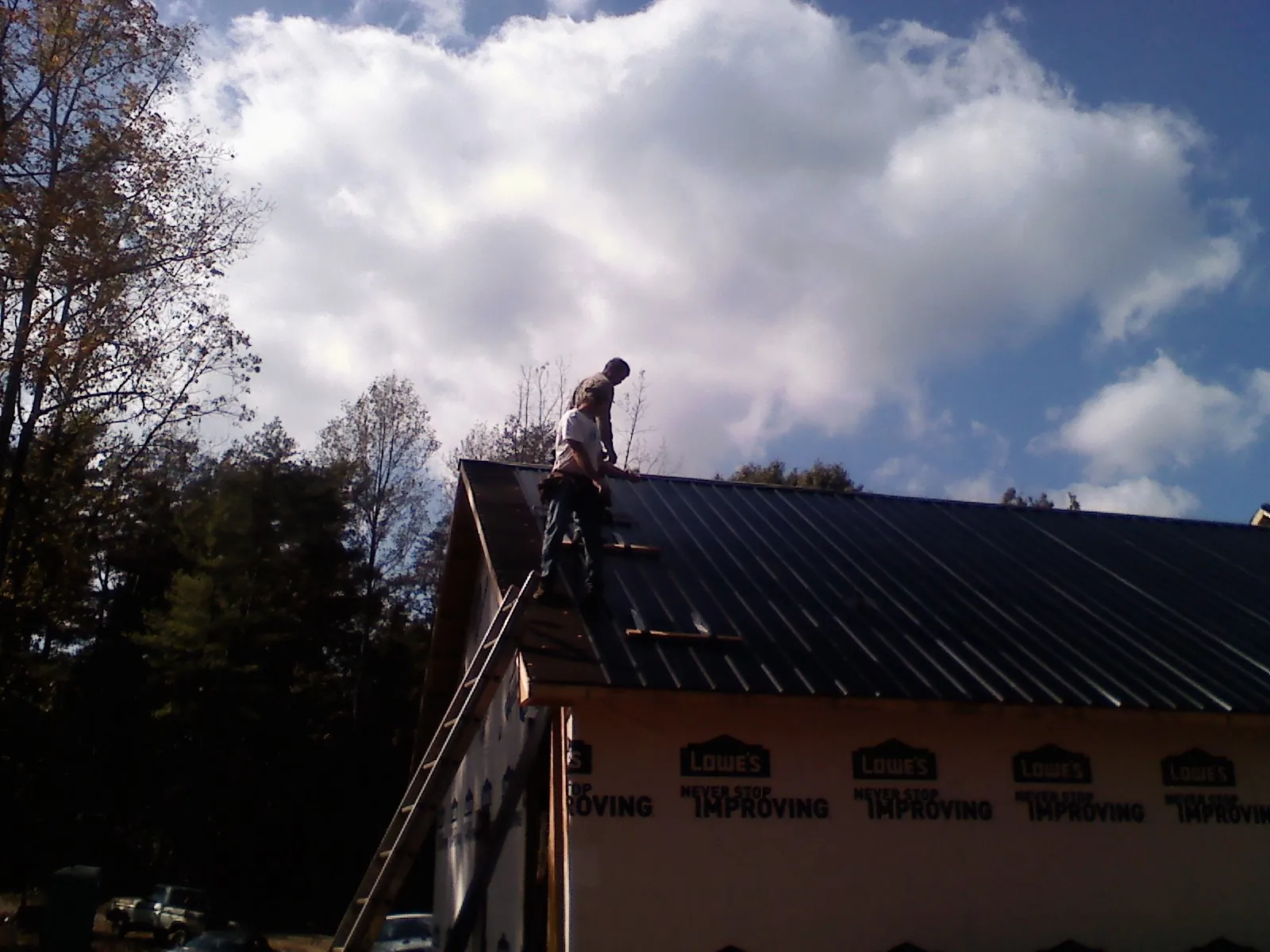 Roofer fastening dark metal panels high against a cloudy sky, from a Roof Inspection job in Coalton