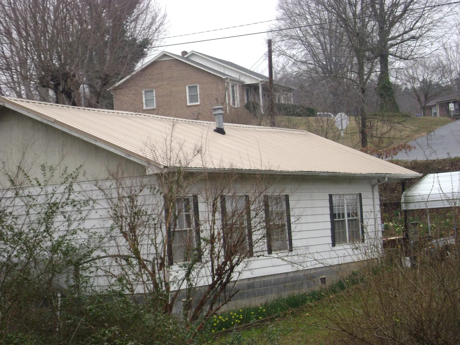 Tan metal roof on a white sided house set into a hillside — Commercial Roofing by Roofing Brothers in Coalton